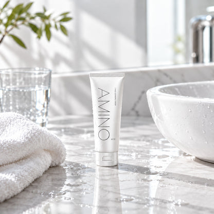 AMINO ACID face cleanser on a white marble bathroom counter beside the basin