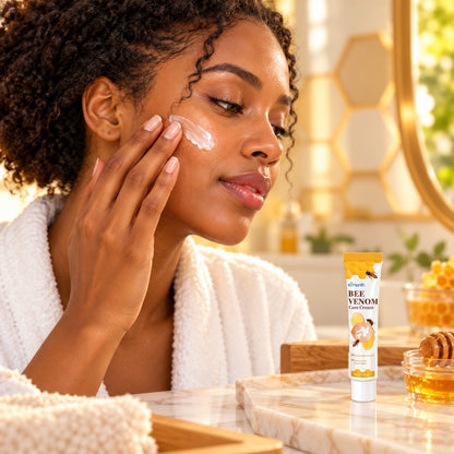 Woman in a bathrobe applying Bee Venom Care Cream at a warm honey-toned vanity