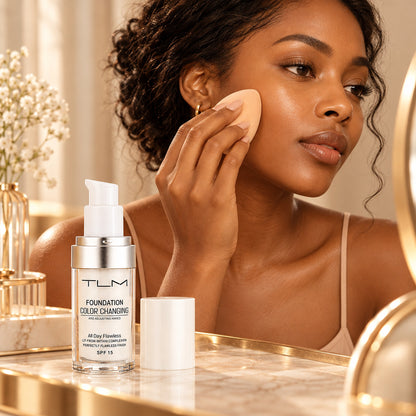 Woman blending the TLM color-adapting liquid foundation onto her cheek with a makeup sponge at her vanity