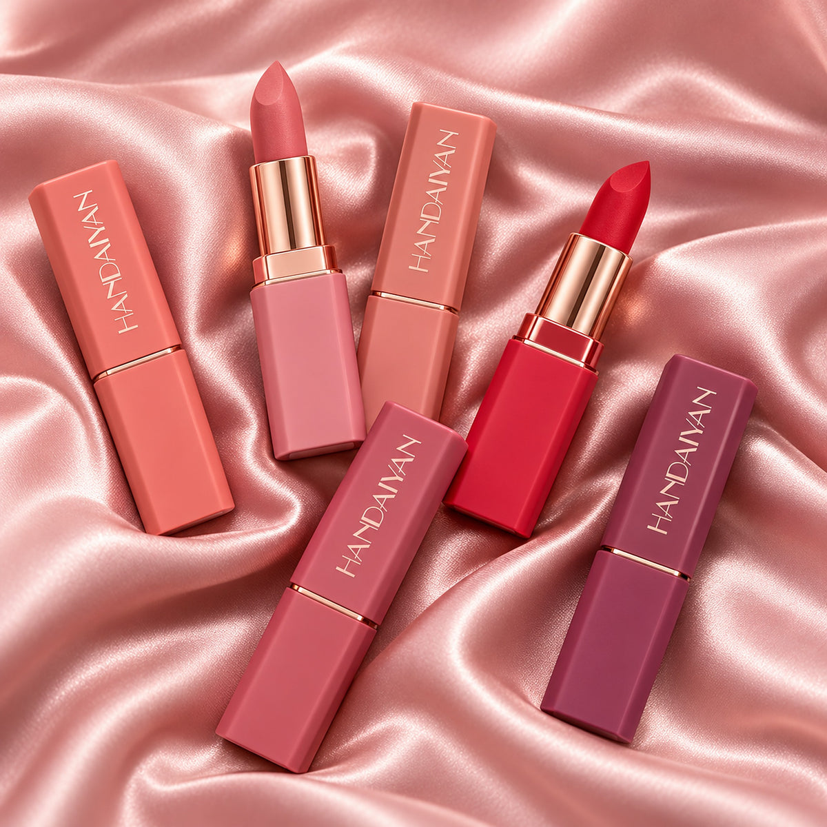 Six HANDAIYAN matte lipsticks fanned out on blush-pink silk, two uncapped