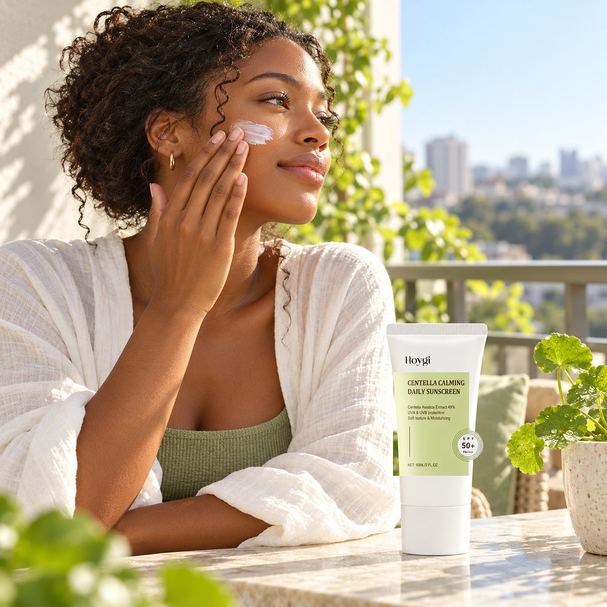 Woman smoothing centella sunscreen onto her cheek on a sunny balcony, Hoygi tube on the table