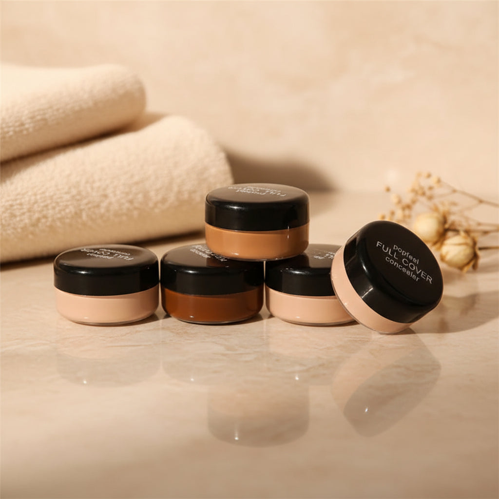 Five POPFEEL Full Coverage Concealer jars on a soft beige marble vanity with a cream towel and dried floral — premium beauty styling.