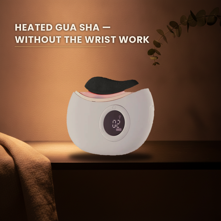Heated gua sha massager on a dark slate ledge with warm spa lighting