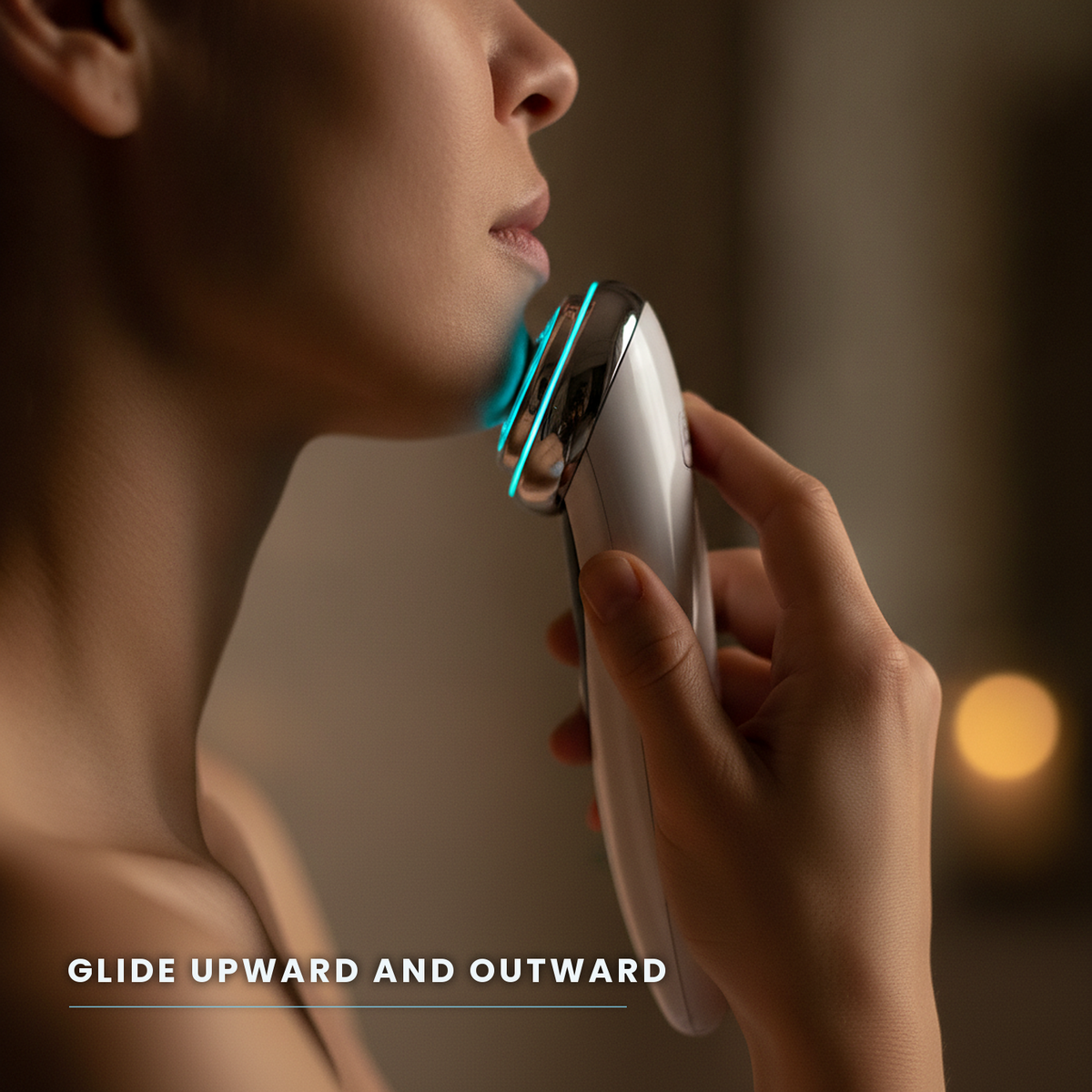 Woman in profile gliding the facial massager upward along her jawline